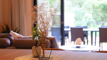 A dining table with a vase of dried plants, a woven placemat, and a view of a dining area with chairs and a table.