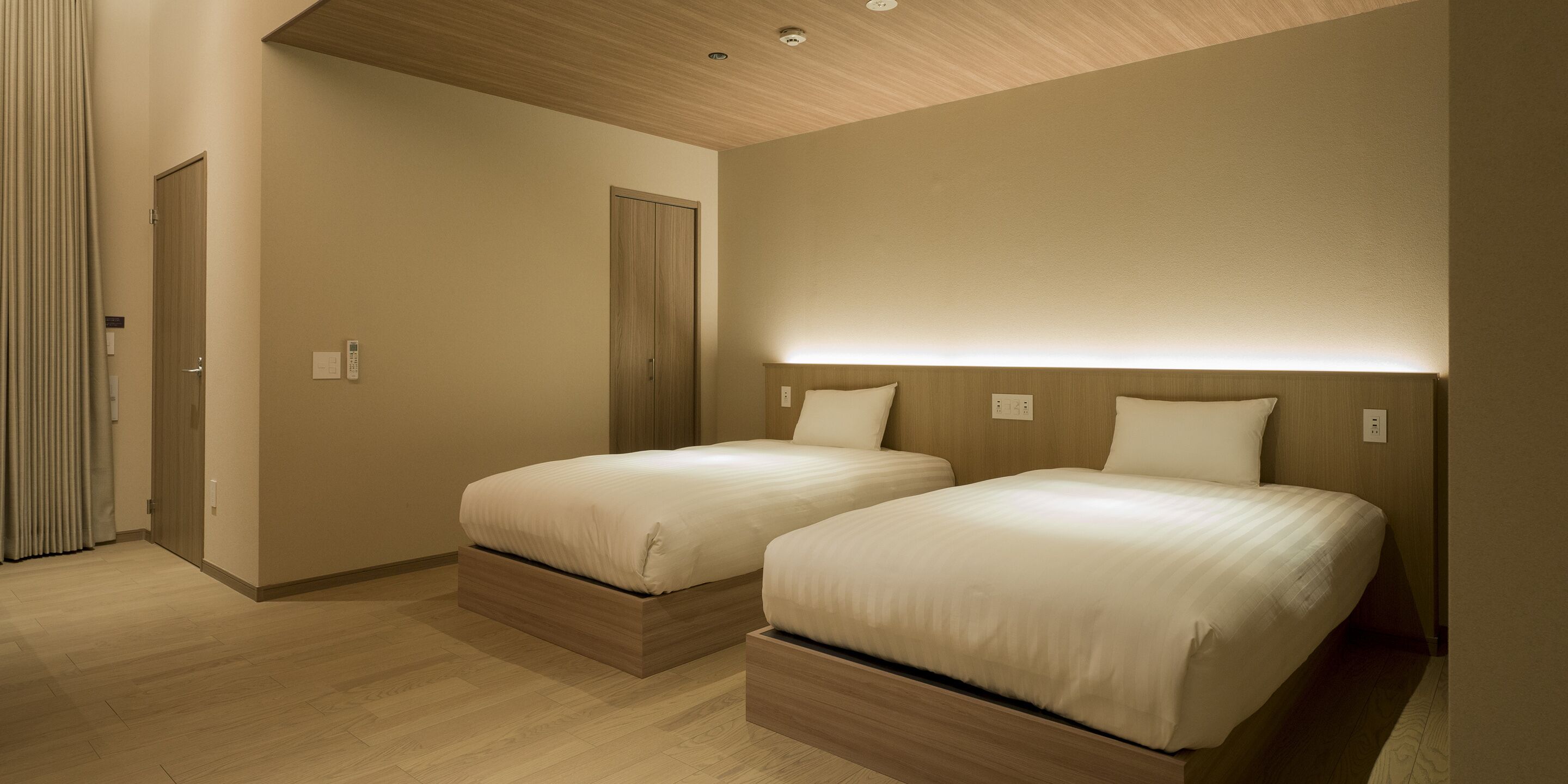 A hotel room with two beds, a wooden ceiling, and a lighted wall panel.