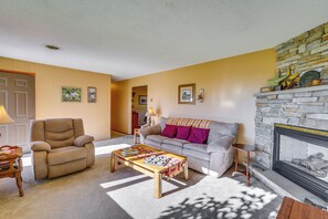 A living room with a sofa, armchair, coffee table, fireplace, and a door.