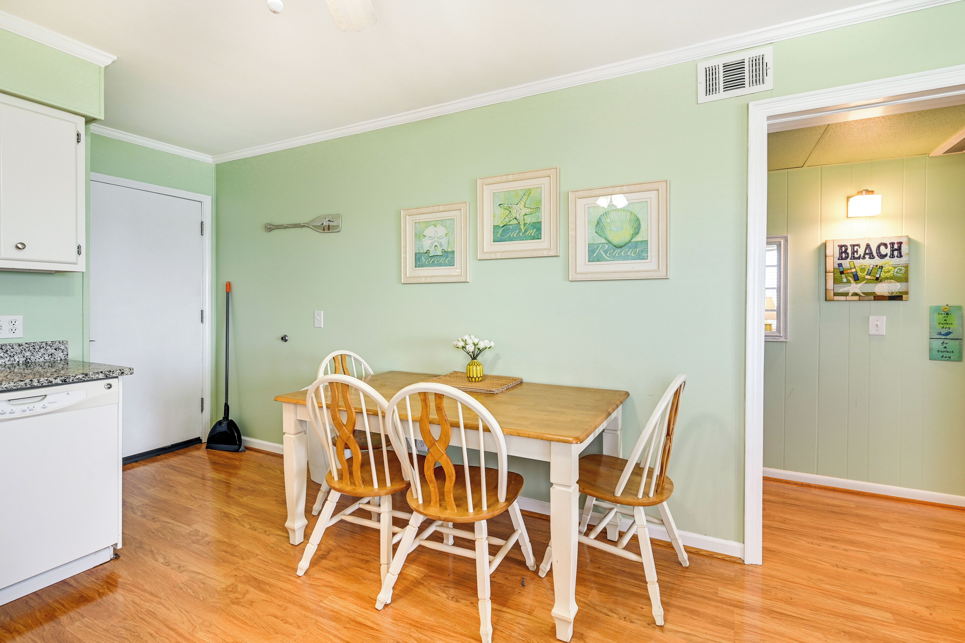 A dining area with a wooden table and four chairs, a kitchen with a dishwasher, and a hallway with a 'BEACH' sign.