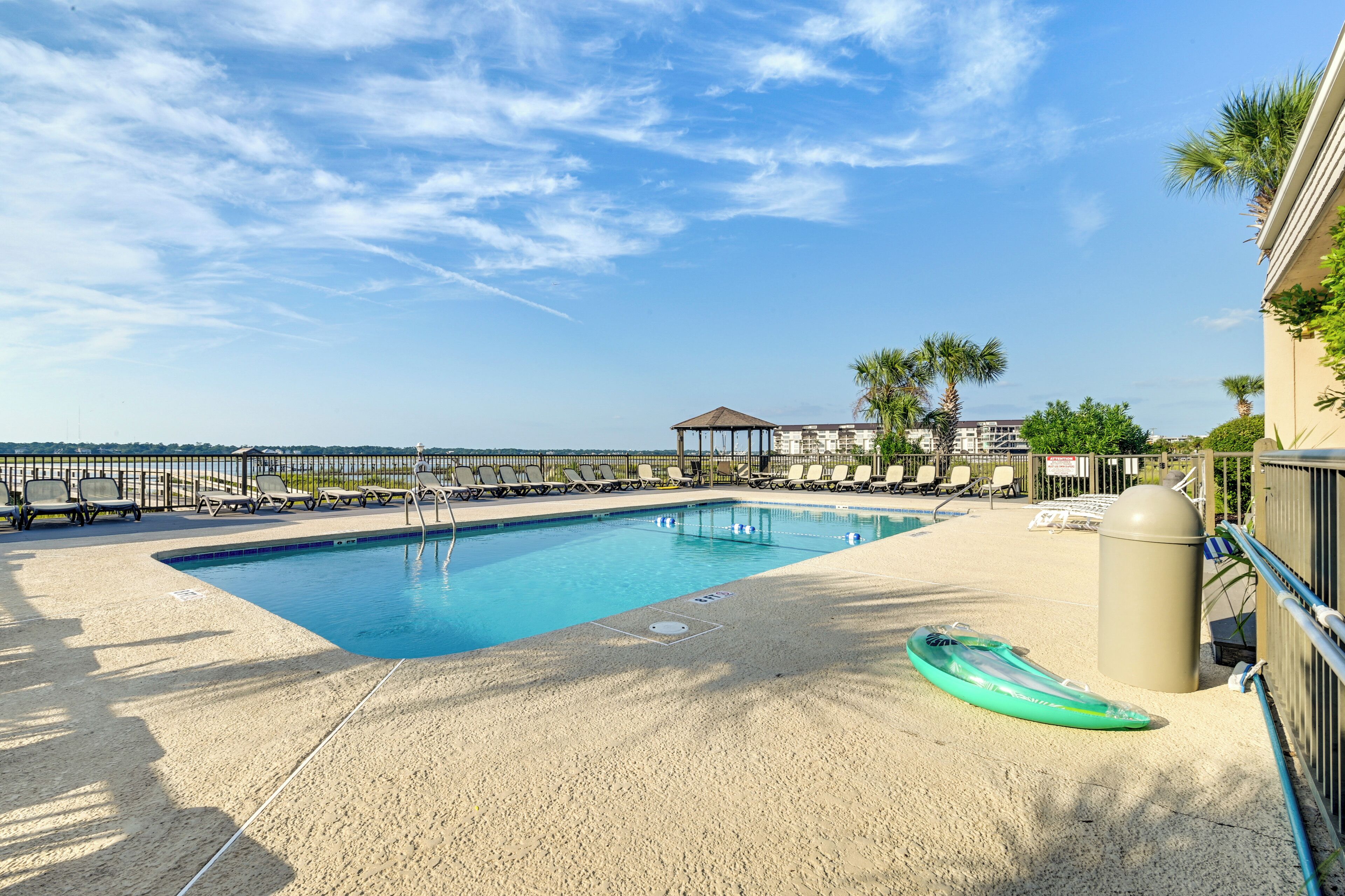 Une piscine rectangulaire bordée d’une plage de sable, entourée de chaises longues et de palmiers.