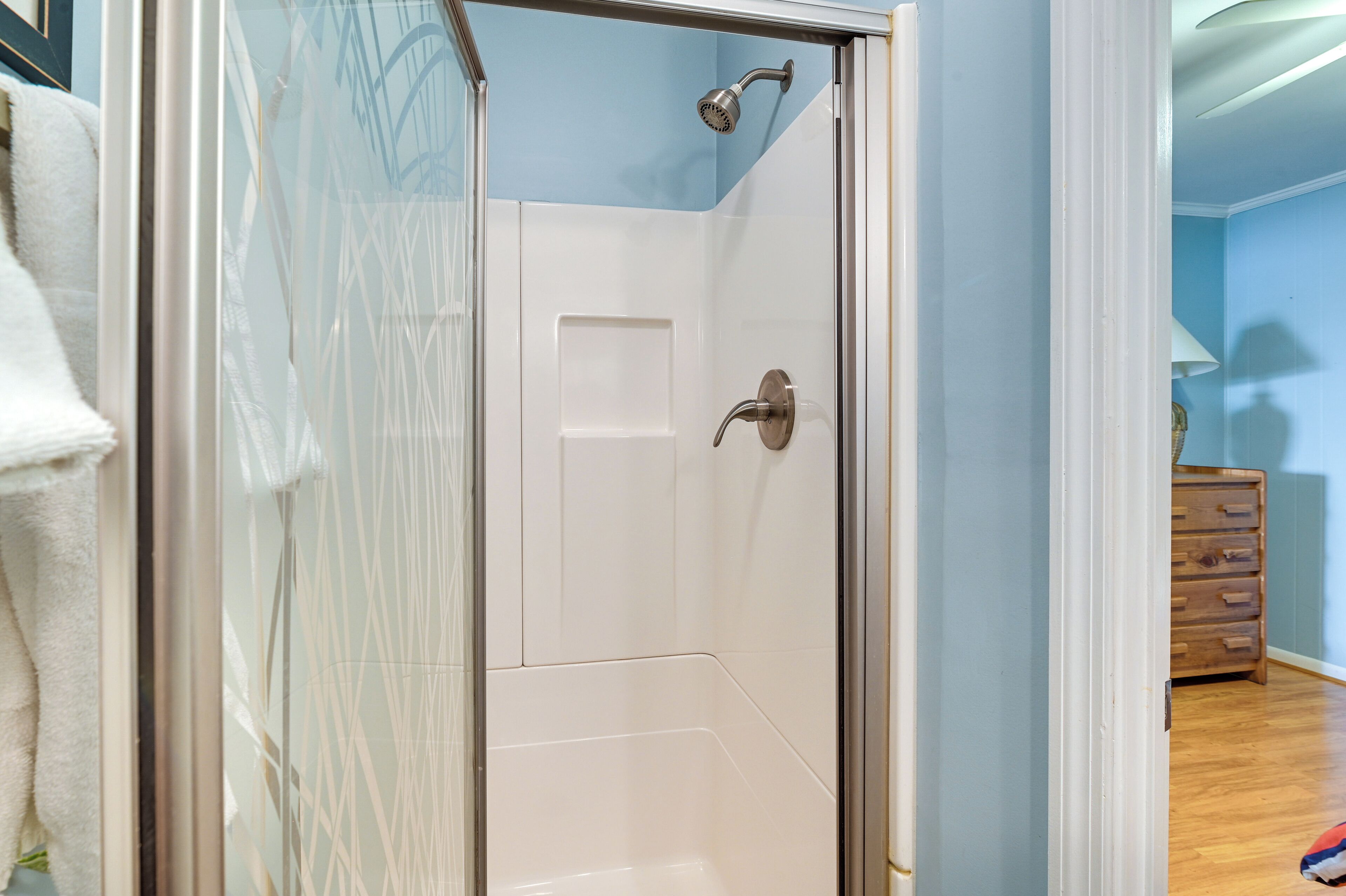 Une douche fermée par des parois de verre, avec une porte blanche et un pommeau de douche.