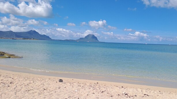 Une plage à l’eau d’un bleu limpide, bordée d’un rivage sablonneux, avec des montagnes qui se dessinent à l’horizon.