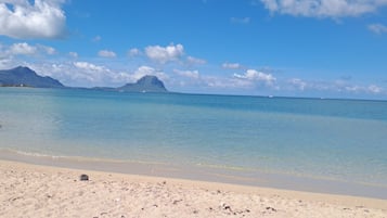 A beach with clear blue water, a sandy shore, and distant mountains.