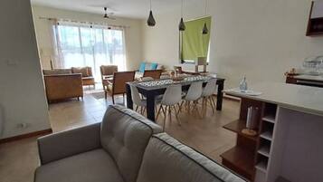 A modern living room with a sofa, dining table, and chairs. There is a kitchen area with a countertop and cabinets.