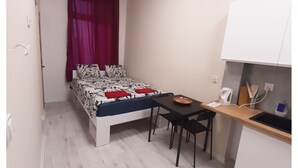 A compact room with a bed, a small table, and a kitchenette.