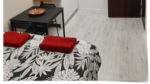 A small kitchenette with a sink, stove, and cabinets. There is a door with a sign, a table with a plate, and a chair.