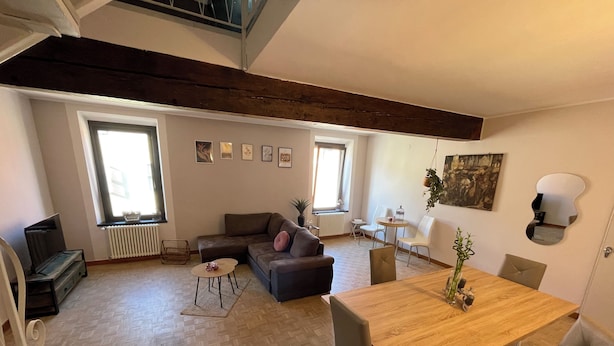 A spacious living area with a wooden dining table, a sofa, and a TV. - Spacious and cozy apartment in historic center (Mantova)