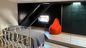 A modern bedroom with a sloped ceiling, a metal bed frame, a red bean bag, and a large window providing natural light. - Spacious and cozy apartment in historic center (Mantova)