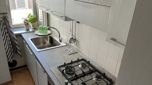 A modern kitchen with white cabinets, a stainless steel sink, and a gas stove. - Spacious and cozy apartment in historic center (Mantova)