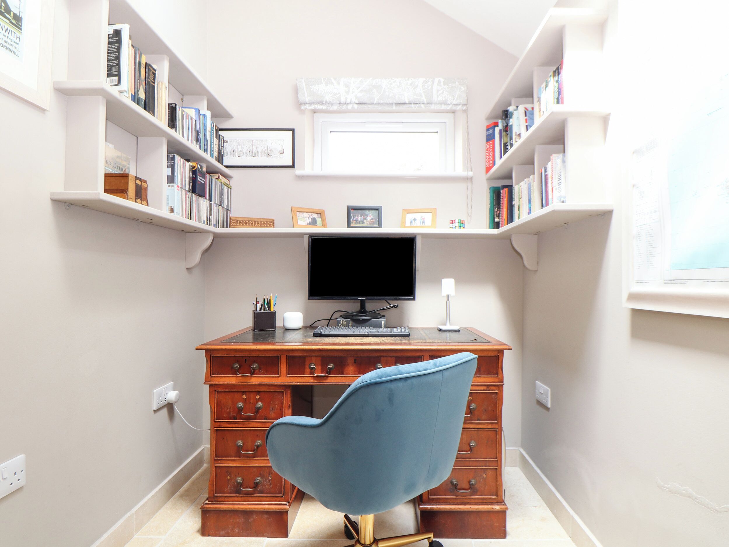 Una sala de estudio con un escritorio de madera, una silla azul, una computadora y estanterías llenas de libros.