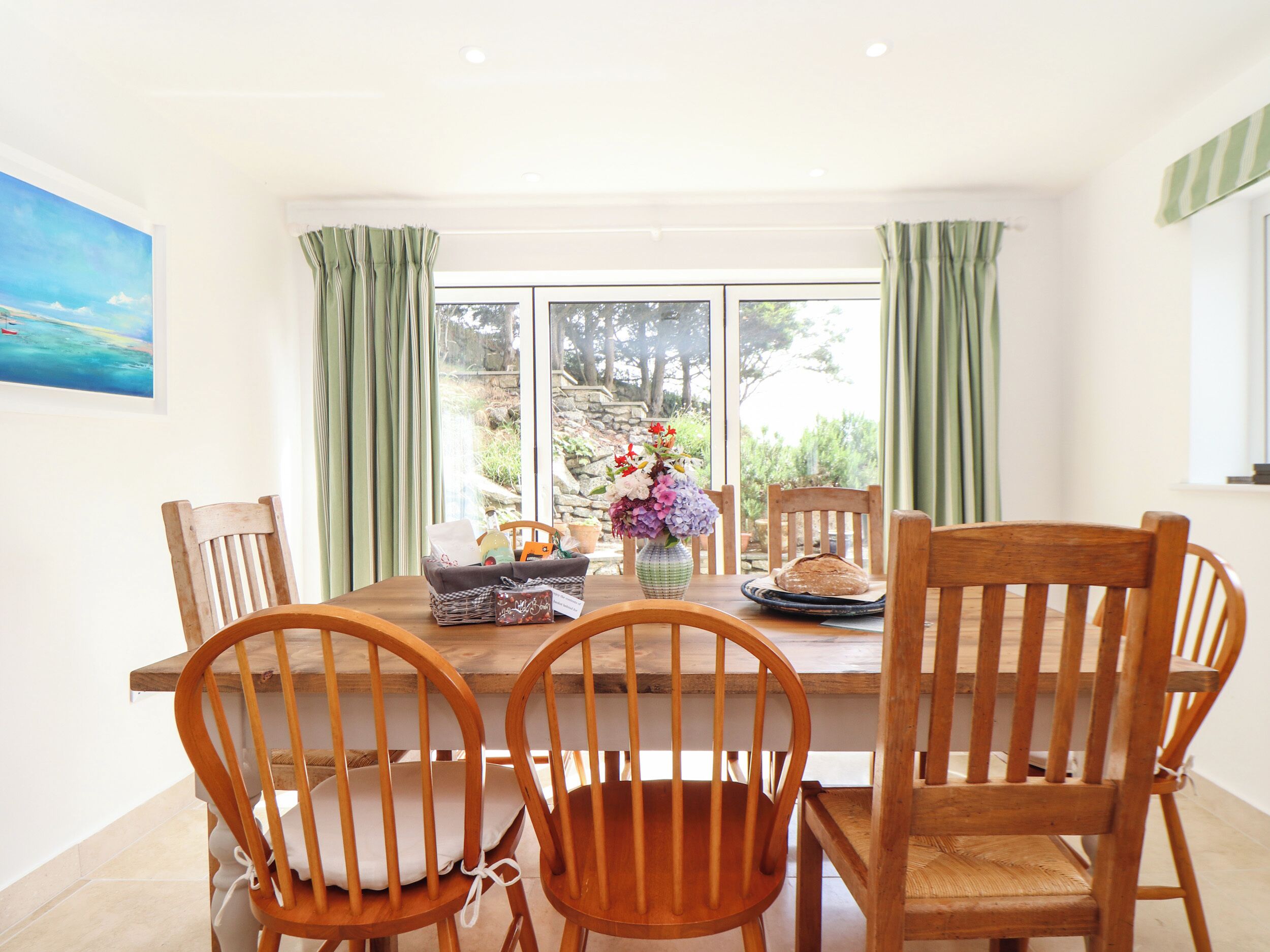 A dining area with a wooden table and chairs, a vase with flowers, and a window with curtains.