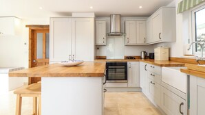 A modern kitchen with white cabinets, a wooden countertop, and an oven. - The Old Barn (Penzance)