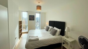 Une chambre moderne avec un grand lit, une table de chevet, une lampe et une vue sur la ville par la fenêtre.