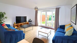 Een moderne woonkamer met een blauwe bank, een televisie en een eettafel.