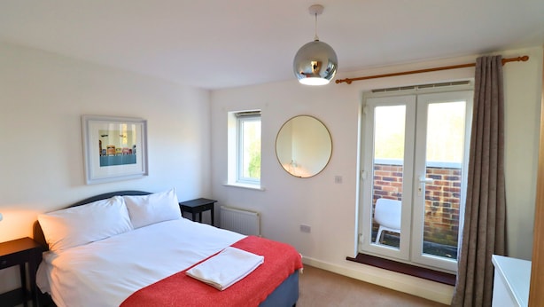 Een slaapkamer met een bed, nachtkastje, spiegel en een raam met gordijnen.