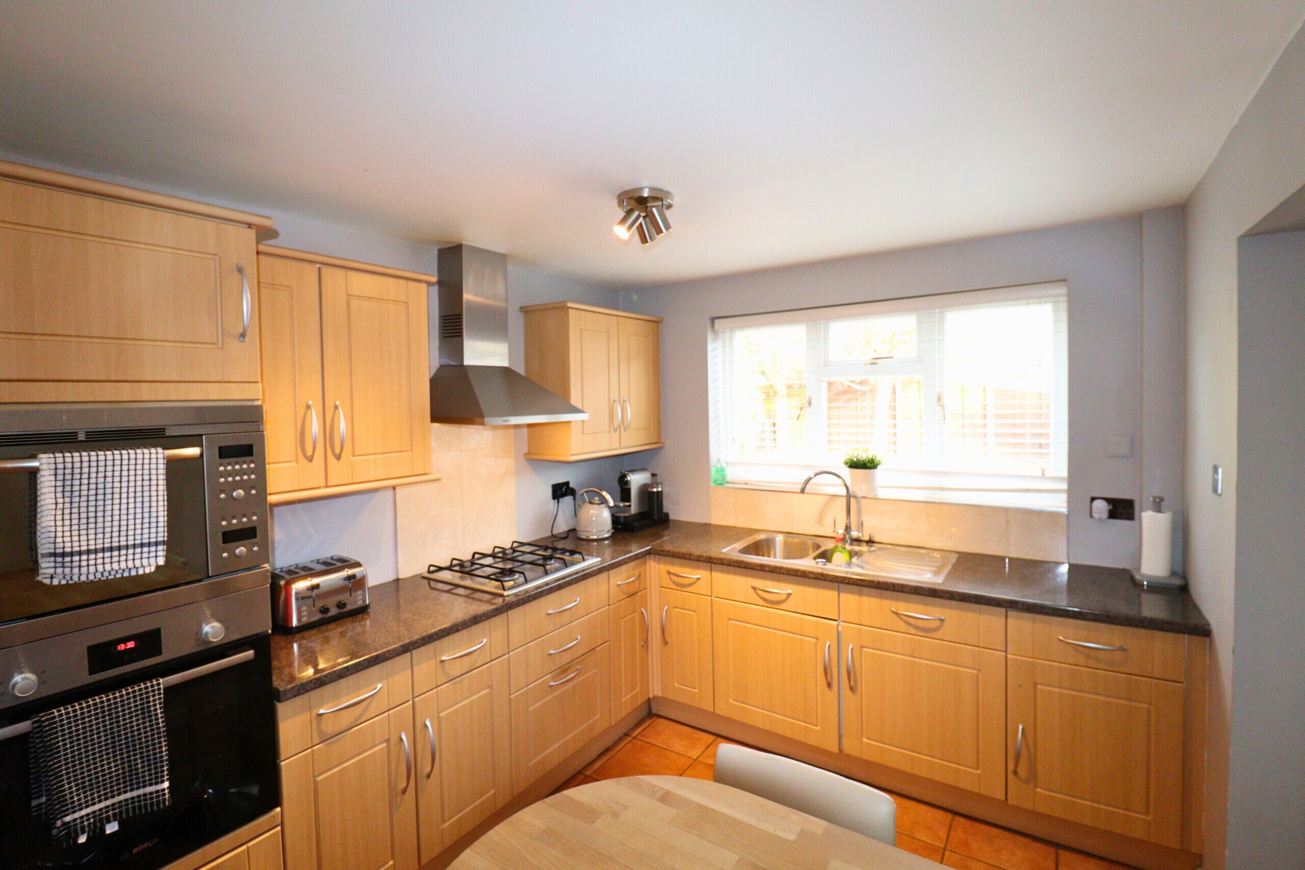 A modern kitchen with wooden cabinets, stainless steel appliances, and a large window providing natural light.