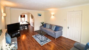 A living room with a sofa, television, and a dining area in the background. - Binfield: Spacious Spectacular Five Bedroom House (Binfield)