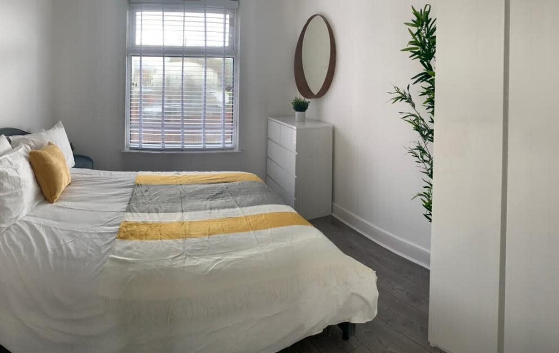 Un dormitorio con una cama, un tocador, un espejo y una planta en maceta.