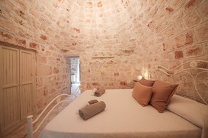 Ein Zimmer mit Stein-Ziegeldecke und -wänden, einem Bett mit weißem Kopfteil und zwei gerollten Handtüchern auf dem Bett.