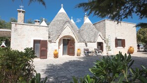 A stone building with a central arched entrance, multiple chimneys, and outdoor seating. - TD I Pagliericci - Enjoy Trulli with Pool (Monopoli)