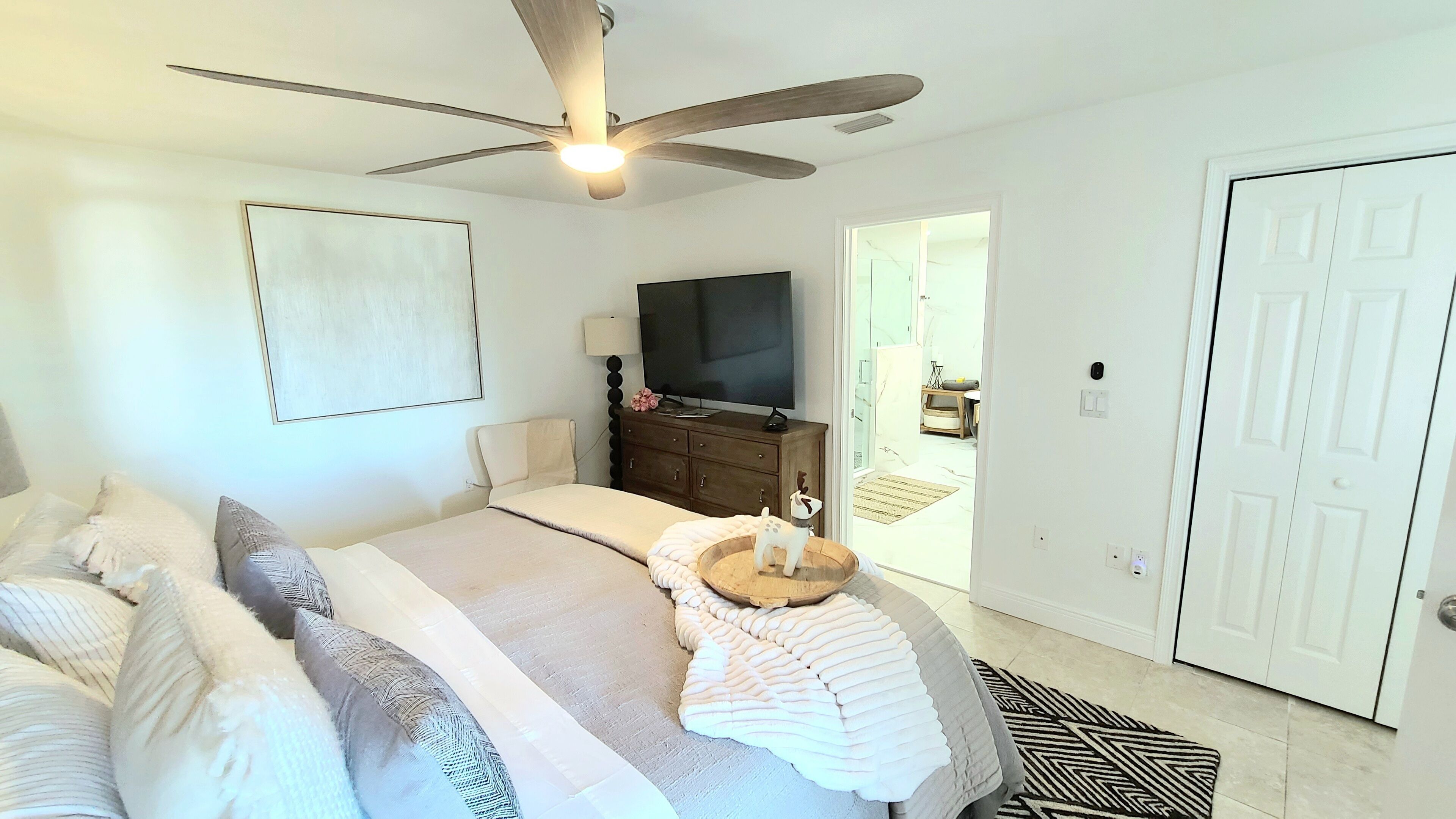 A bedroom with a bed, a ceiling fan, a TV, a dresser, and a door.