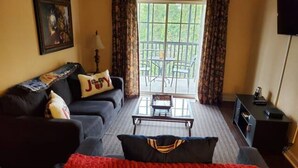 A room with a sofa, a red blanket, a coffee table, and a view of the outdoors through a window.