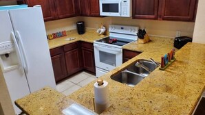 A kitchen with granite countertops, a white refrigerator, a microwave, an oven, and a sink.