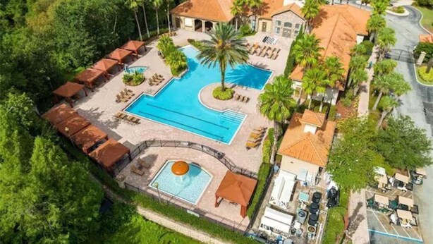 An aerial view of a resort with a large swimming pool, lounge areas, and a parking lot.