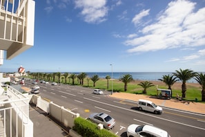 A coastal road with a view of the sea, palm trees, and a bus stop.