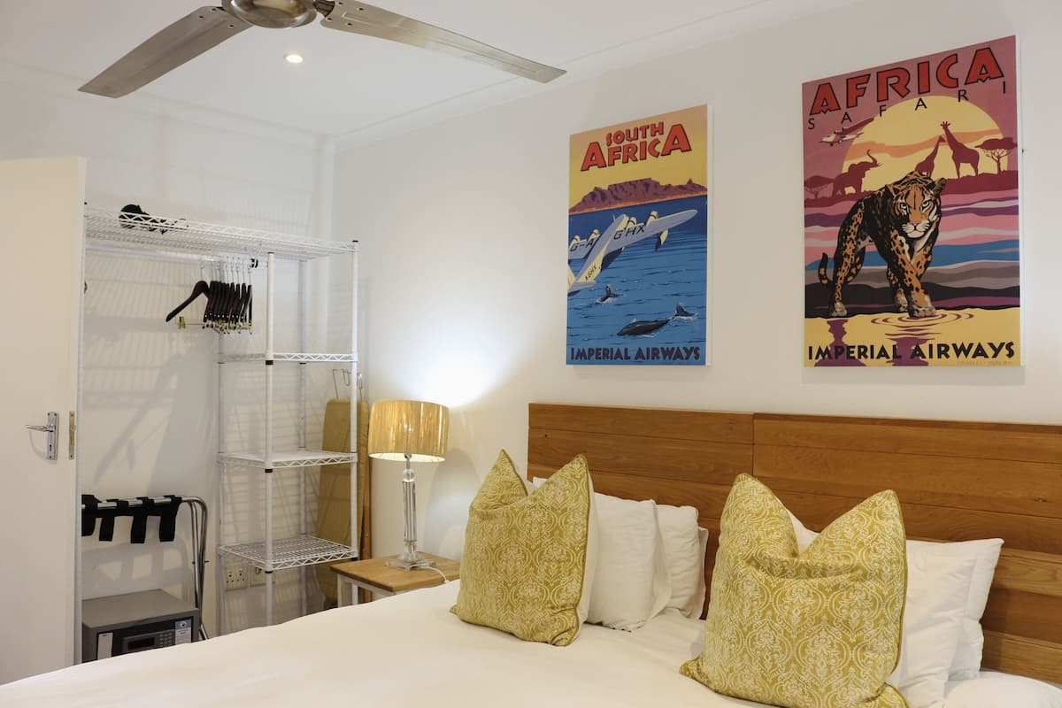 Une chambre d’hôtel avec un lit, des oreillers, une table de chevet, une lampe, une armoire et deux affiches au mur.