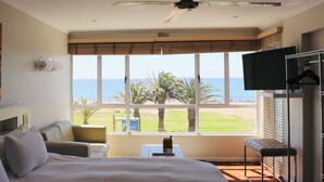 Een hotelkamer met een groot bed, een plafondventilator, een televisie en uitzicht op het strand.