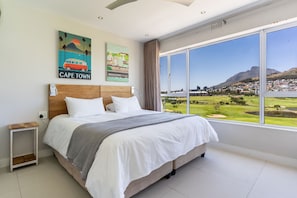 A hotel room with a large bed, a nightstand, and a window with a city view.