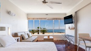 Een moderne hotelkamer met een groot bed, een sofa, een televisie en een balkon met uitzicht op het strand.