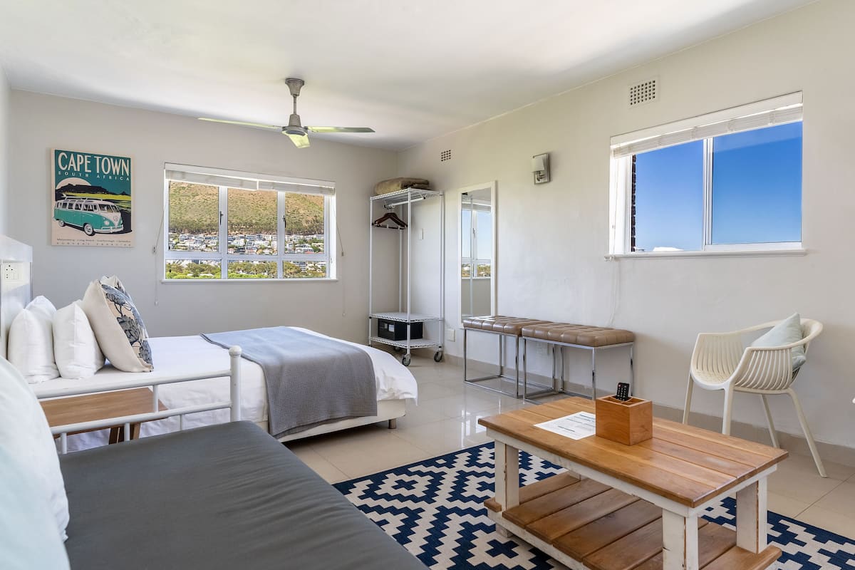 Une chambre moderne et bien éclairée, équipée d’un lit, d’un bureau, d’une chaise et offrant une vue sur Le Cap.