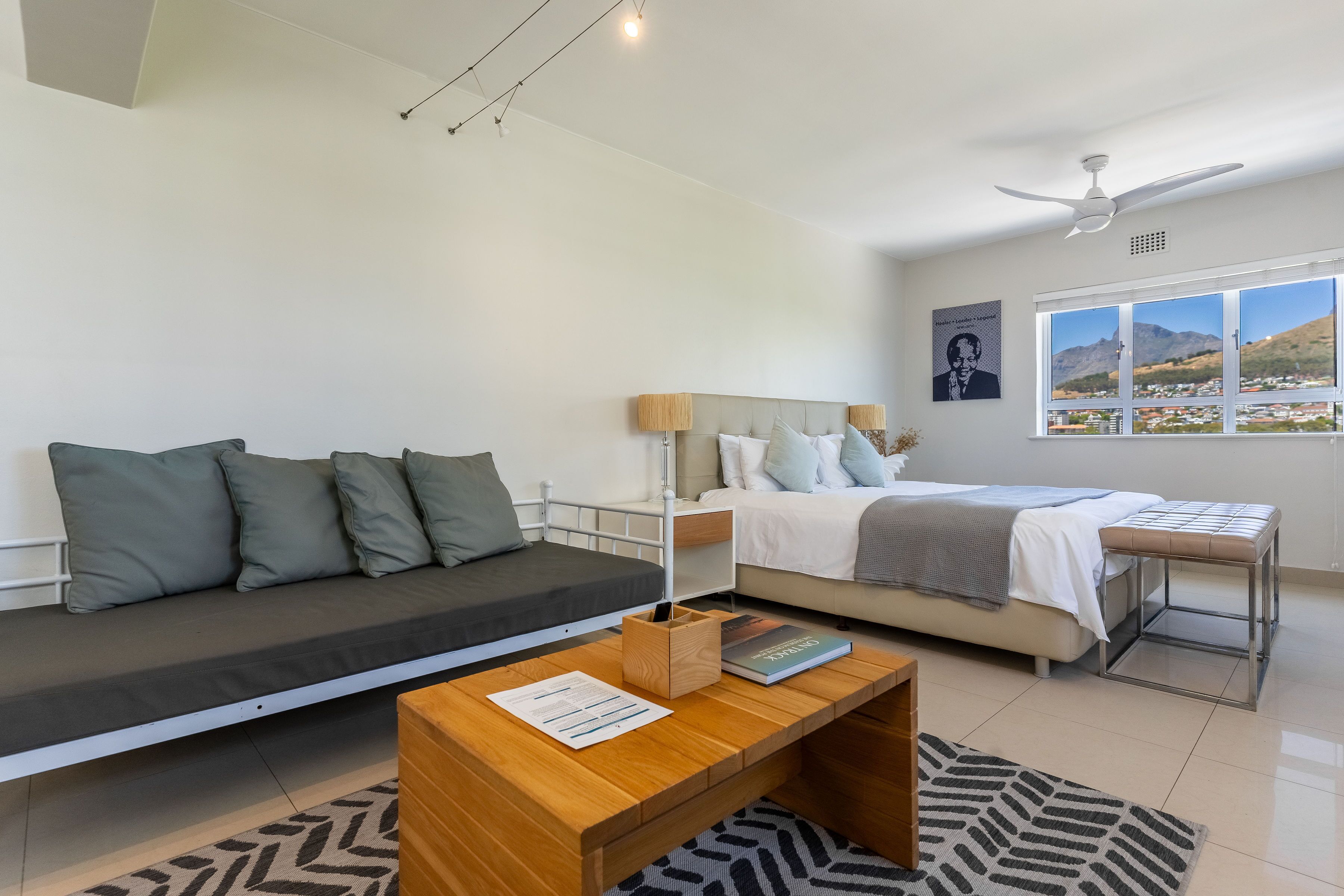 Un dormitorio moderno con sofá cama, una cama individual, una mesa de centro de madera y vistas a la montaña a través de la ventana.