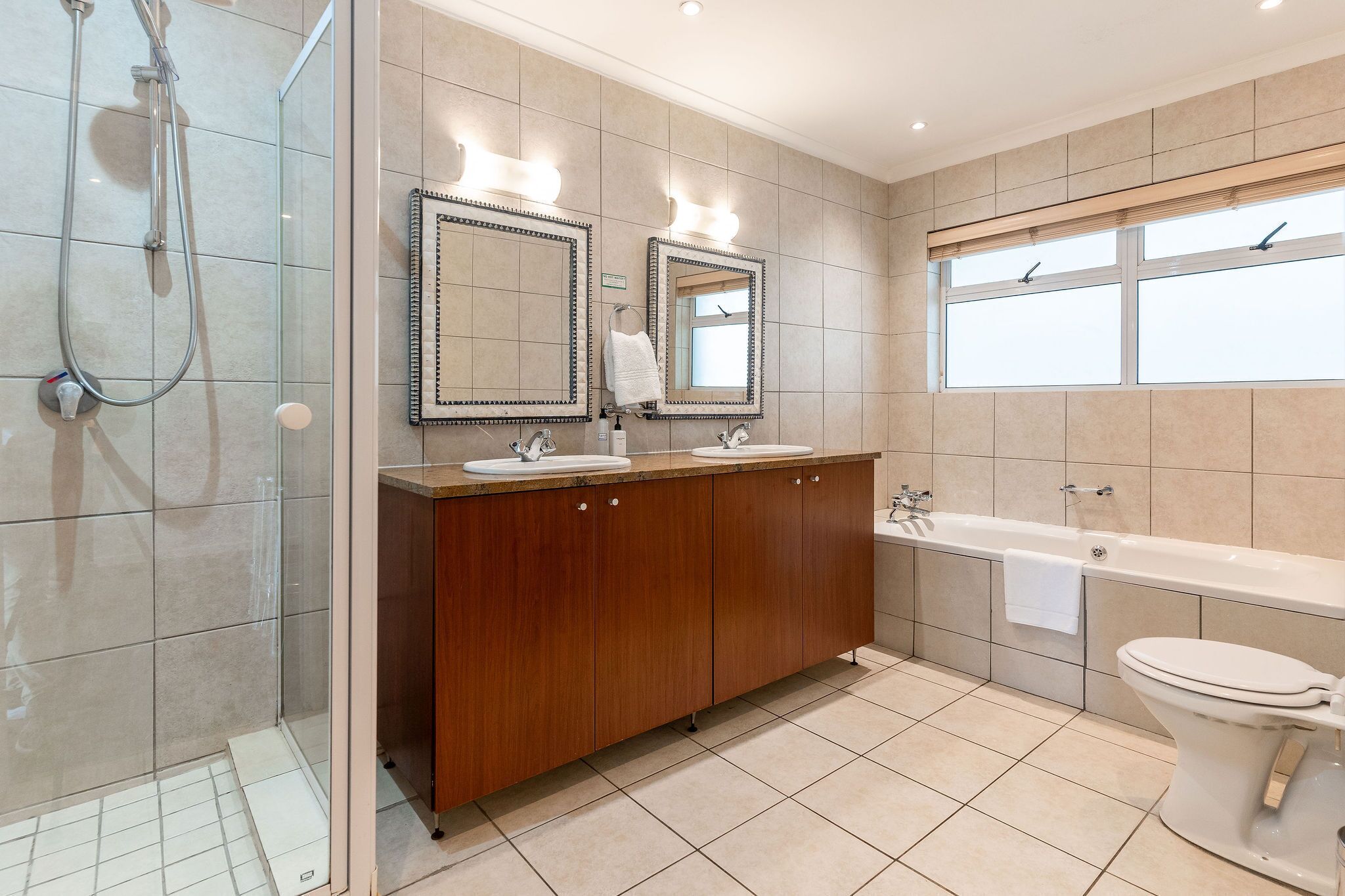 A modern bathroom with a glass-enclosed shower, double sinks, a bathtub, and a toilet.