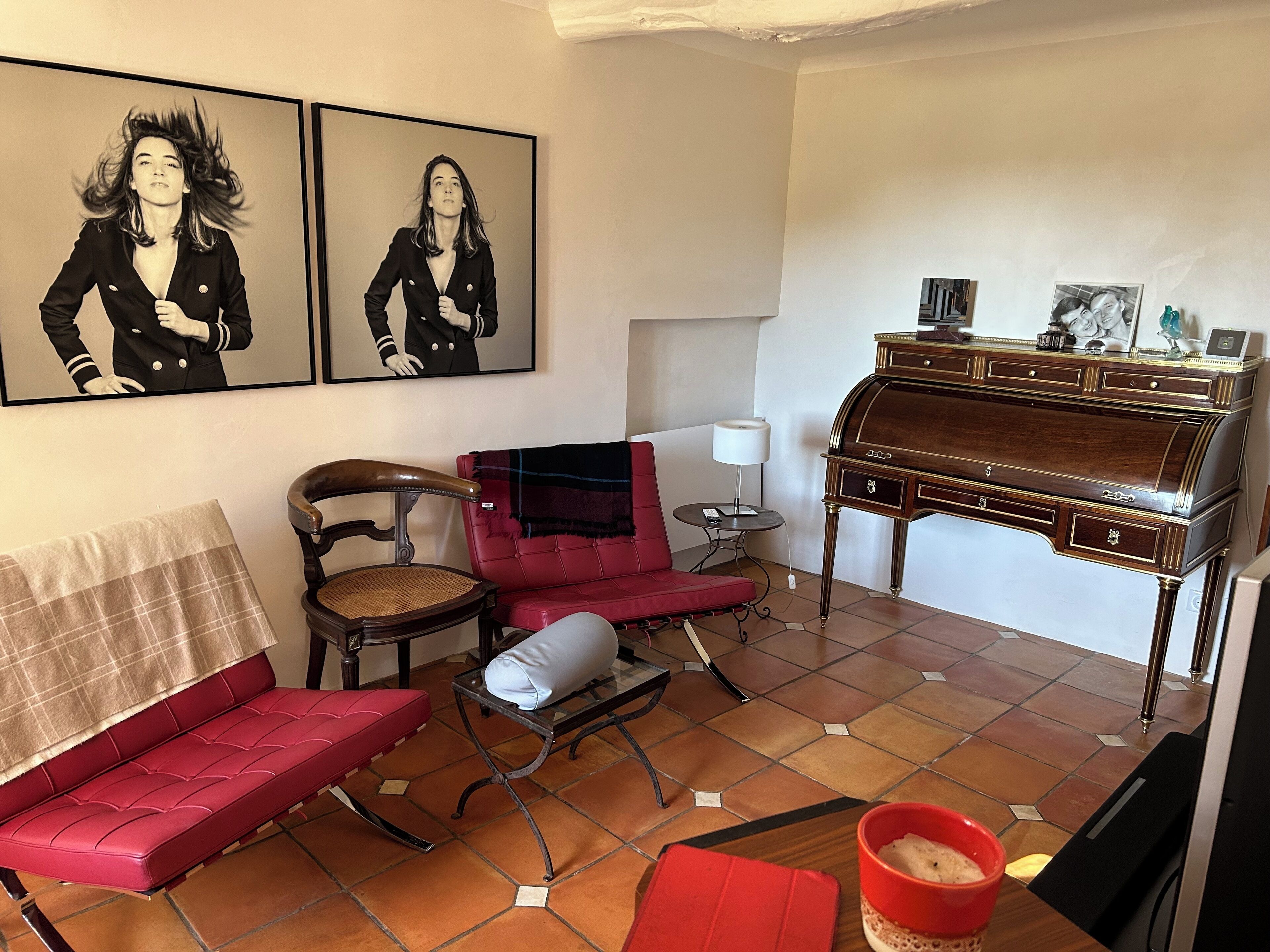 Ein Wohnzimmer mit einem roten Sofa, einem Holzstuhl, einem roten Sessel, einem kleinen Tisch mit Lampe, einem Holzpiano und zwei gerahmten Bildern an der Wand.