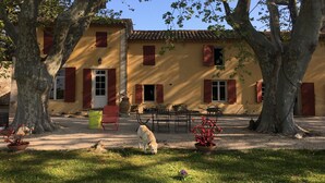 A yellow building with red shutters, surrounded by trees and a dog. - Mas provençal with tennis court, swimming pool and games and sports room (Velaux)