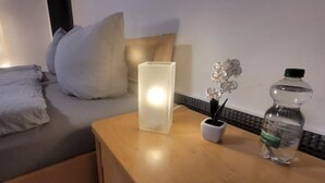 A hotel room with a bed, a bedside table with a lamp, a bottle, and a small potted plant. - Villa Souterrain, W-lan, Büro (Leverkusen)