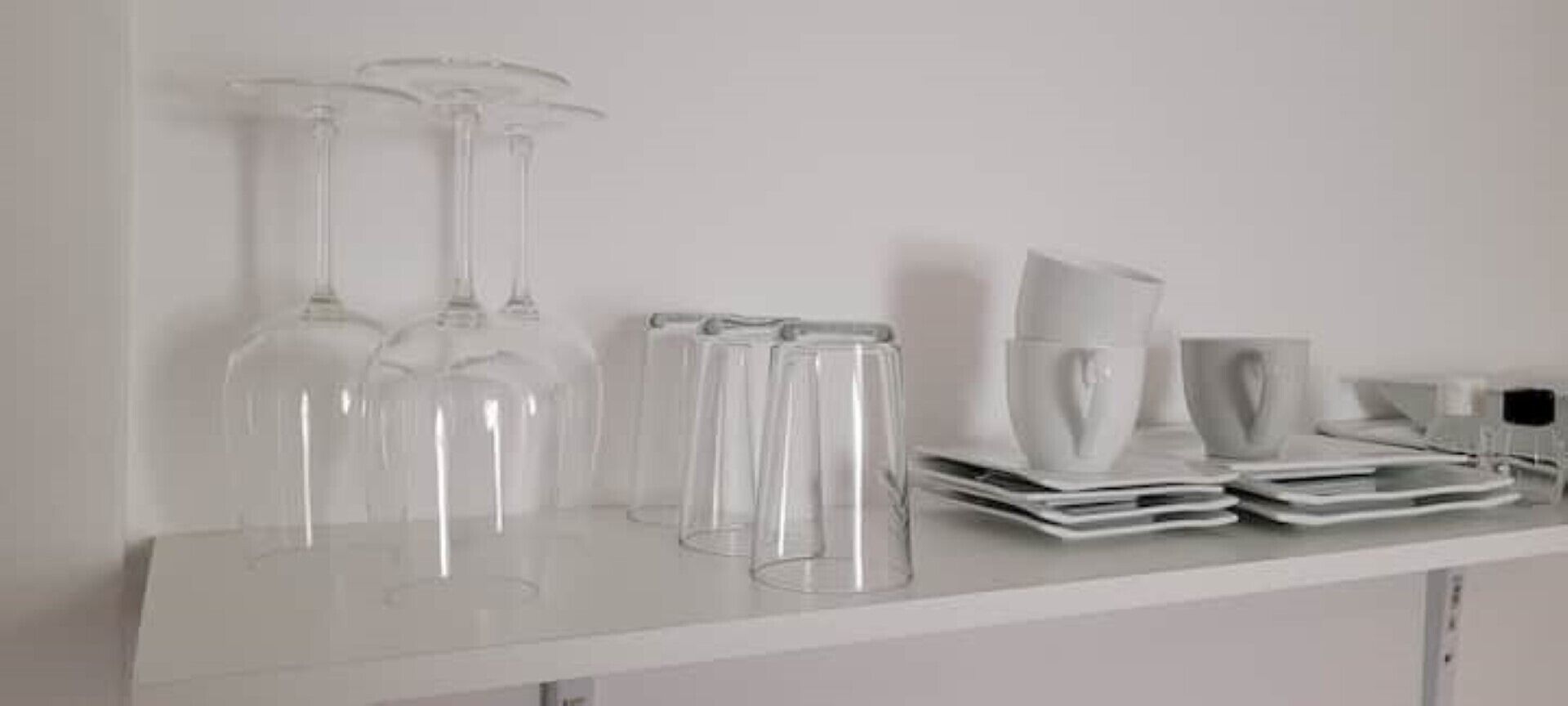 Una estantería blanca con cristalería transparente y platos blancos.