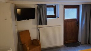 A room with a wooden door, a window with curtains, a radiator, a television mounted on the wall, and a wicker chair. - Villa Souterrain, W-lan, Büro (Leverkusen)