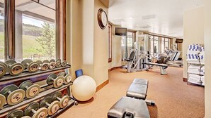 Un gimnasio con equipo de ejercicio, un reloj y una ventana con vistas a la vegetación.
