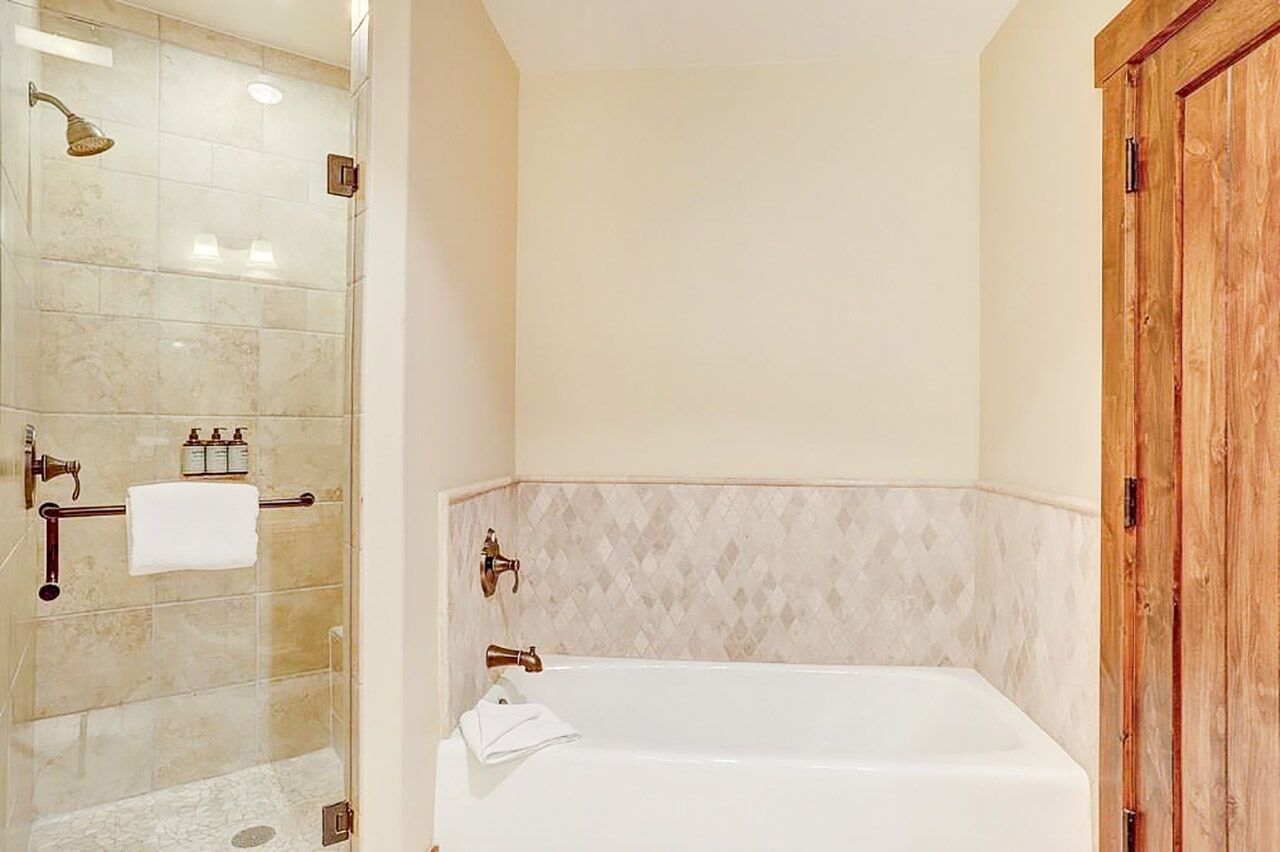 Une salle de bain avec une douche à parois de verre, une baignoire blanche et une porte en bois.