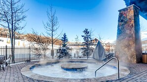 Un jacuzzi con un pilar de piedra y vista a un paisaje nevado.