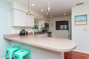 A kitchen with white cabinets, a central island with stools, a microwave, and a window with a view. - Tranquil Waters, OceanPines, 3 br, Dog Friendly (Ocean Pines)