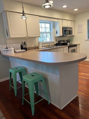 A kitchen with white cabinets, a central island with stools, a microwave, and a stove. - Tranquil Waters, OceanPines, 3 br, Dog Friendly (Ocean Pines)