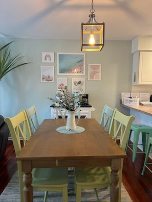 A dining area with a wooden table, green chairs, a vase with flowers, and artwork on the walls.