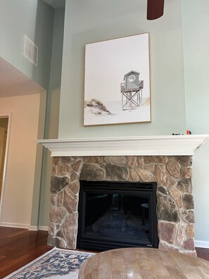 A living room with a stone fireplace, a framed picture above the mantel, and a patterned rug on the floor. - Tranquil Waters, OceanPines, 3 br, Dog Friendly (Ocean Pines)