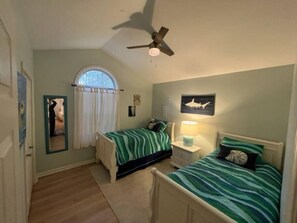 A bedroom with two beds, a ceiling fan, a window with curtains, and a framed picture on the wall.